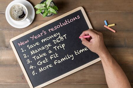 Hand man writing New year resolution on black board with coffee and wood background, New year goal ...