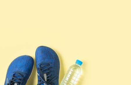 Blue running shoes and bottle of water on yellow background, sport and healthy concept.の写真素材