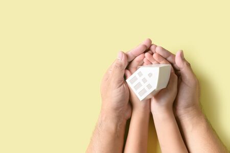 Father and child hand holding little model house in hands isolated on yellowの写真素材