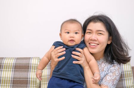 Happy asian mother holding baby in her arms and sit on sofaの写真素材