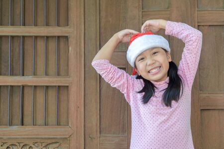 Cute asian girl wearing santa hat smile on old wood wall background, Christmas concept.の写真素材