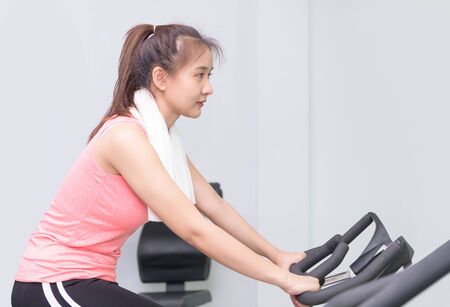 Fit asian young woman using exercise bike at the gymの写真素材