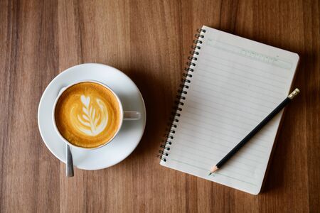 cup of latte art coffee with blank notebook and pencil on wooden background, selective focus