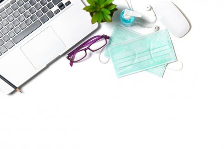 White office desk table with surgical face mask and sanitizer bottle or alcohol gel with laptop isolated on white background, work from home and covid-19 conceptの写真素材