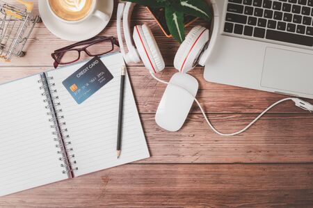 credit card on blank note book with pencil on wooden office desk consisting of a laptop, headphones...