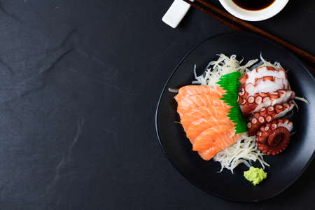Salmon and Tako sashimi on black dish with chopsticks, Japanese food, black stone table background and copy spaceの写真素材