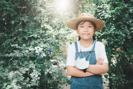 Farmer girl wearing denim overalls with hat and hanging a mask in the vegetable garden.の写真素材