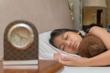 Cute little girl hugging teddy bear sleeping lay in  bed, happy small child embracing toy fall...
