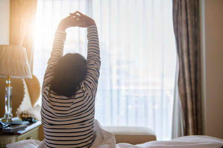 Little girl is stretching on bed after waking up with sunrise at morning, back view. Good morning world conceptの写真素材