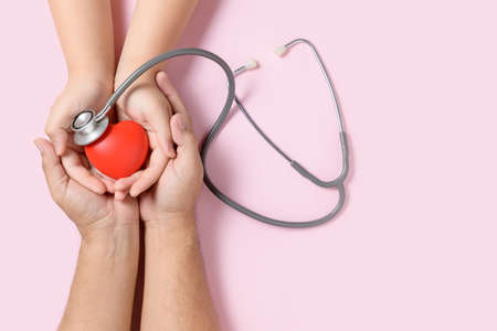 Hand child holding red heart and stethoscope isolated on pink background, organ donation, happy...