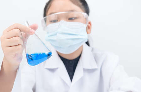 A little scientist is looking at blue liquid chemical in beaker isolated on white background. Science experiment and education conceptの写真素材