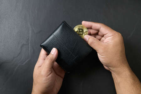 Businessman putting bitcoin into a black leather wallet on black background. saving bitcoin concept....