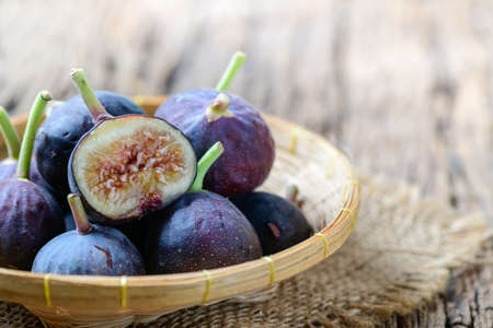 Fresh purple fig fruit and slices isolated in bamboo basket on old wood background, Figs are high in calcium and contains anti-oxidants It helps prevent constipation and helps alleviate diabetes.の写真素材