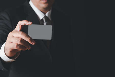 businessman in black costume and gray necktie  showing gray card on black background. Payment banking conceptの写真素材