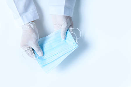 Doctor hands in medical gloves holding surgical  protective mask isolated on white background. Prevent and help stop the  virus outbreak concept, Top view.の写真素材