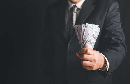 Businessman hand grabbing money, US dollar (USD) bills on black background, investment, success and...