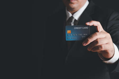 businessman in black costume and gray necktie  showing credit card on black background. Payment banking conceptの写真素材
