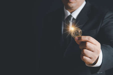 business man wearing suit and necktie holding bit coin on black background,electronic virtual money for web banking and international network payment,の写真素材