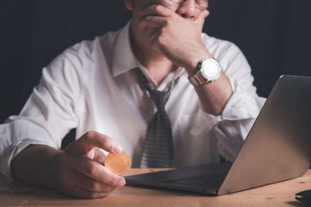 businessman hold Bitcoin and watches the laptop with stress due to losses from trading Bitcoin.