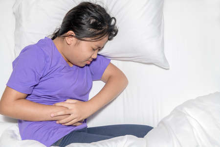 Asian child suffering from stomachache and lying on bed.