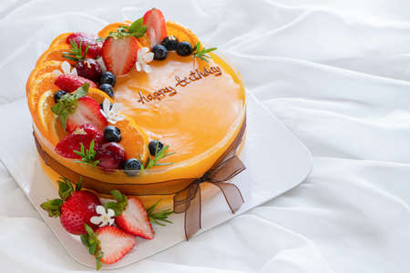 Orange cake with happy birth day and topped with orange, strawberry, blueberry