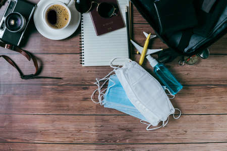 Prepare mask and alcohol spray near suitcase, vintage camera, notebook, map  on wood and copy space. travel and prevent  concept