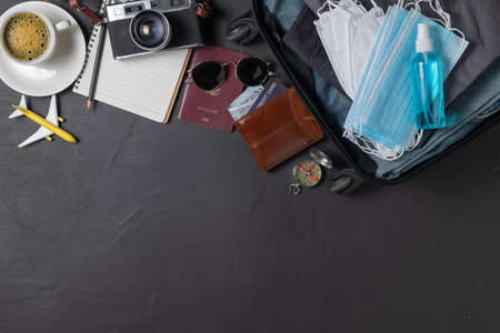 Prepare mask and alcohol spray in suitcase, vintage camera, notebook, map  on black table and copy...