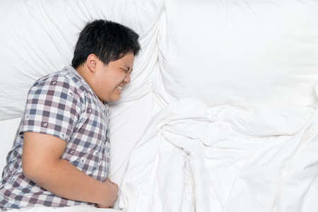 Asian fat boy lying in bed. His hand holding the stomach.の写真素材