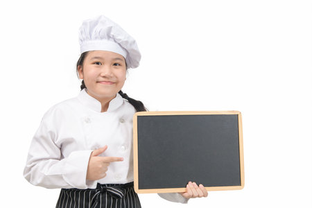 Little asian girl chef in uniform cook holding blackboard for in put text or menu, isolated on white backgroundの写真素材