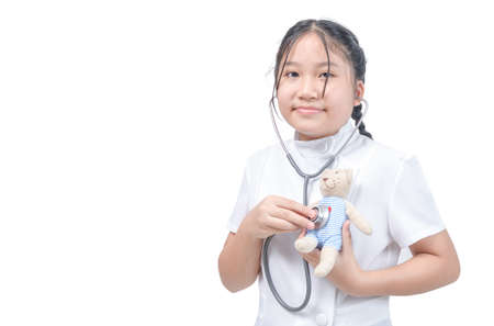 CUte little girl playing doctor and listening teddy bear with stethoscope isolated on whiteの写真素材