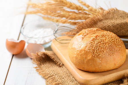 Sourdough Bread with Sesame on wood plated and Whisk, flour and eggshells on white wood background, Homemade bakery concept.の写真素材