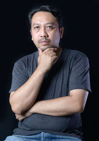 Smart middle-aged man with bearded wearing a gray t-shirt on black background. Thinking concept