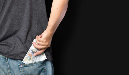 Man hides dollar bills in back pocket of jeans, corruption concept