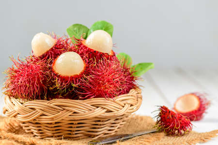Fresh Rambutan fruits with leaves in bamboo basket on wood background. fruit Southeast Asia in summer seasonの写真素材