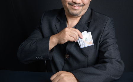 Man putting bribe money into pocket on black background, Concept for corruption, finance profit, bail and crimeの写真素材