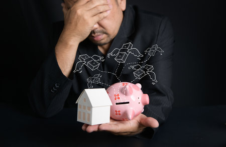 paper house and piggy bank on hand on black background, Businessman stressed about money to buy a new house, saving money conceptの写真素材