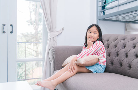 Happy asian little girl sitting on sofa in living room at homeの写真素材