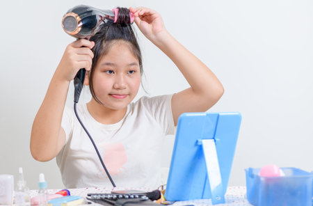 cute girl wearing hair rollers and holds a hair dryer and look at the mirror isolated on white background,の写真素材