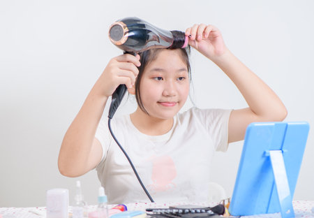 cute girl wearing hair rollers and holds a hair dryer and look at the mirror isolated on white background,の写真素材