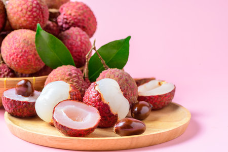 Juicy Lychee with cut in half and leaves on wood plate isolated on pink background. Thai fruits conceptの写真素材