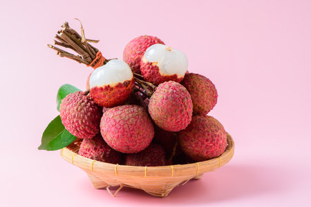 Juicy Lychee with cut in half and leaves on bamboo basket isolated on pink background. Thai fruits conceptの写真素材