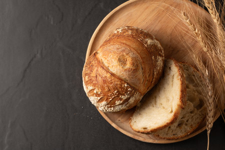 Top view of a freshly baked, crusty artisanal sourdough loaf, presented on a rustic wooden plate. A...
