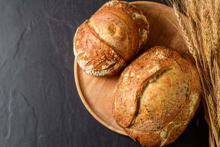 Top view of a freshly baked, crusty artisanal sourdough loaf, presented on a rustic wooden plate. A...