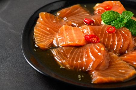 Close-up of Korean soy marinated salmon slices served on a black plate with red chili and fresh mint. Popular Korean dish known as salmon jang, raw seafoodの写真素材