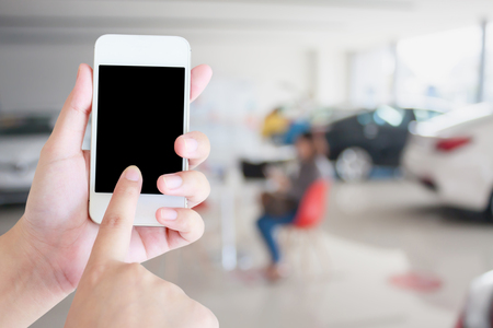 hands holding mobile phone with new cars in showroom dealershipの写真素材