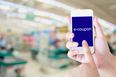 Hand holding mobile phone at supermarket checkout background, e coupon conceptの写真素材
