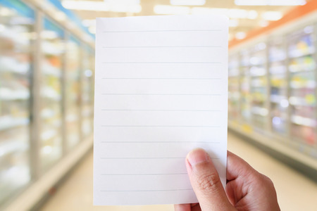 hand hold white paper over supermarket aisle with refrigerators blurred backgroundの写真素材