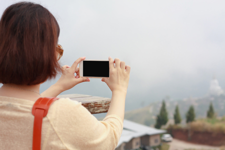 Back view of woman taking photograph with smart phone camera at the mountainの写真素材