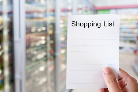 hand holding shopping list paper with convenience store shelves blurred backgroundの写真素材