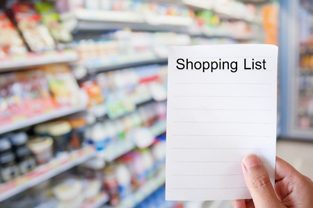 hand holding shopping list paper with convenience store shelves blurred backgroundの写真素材